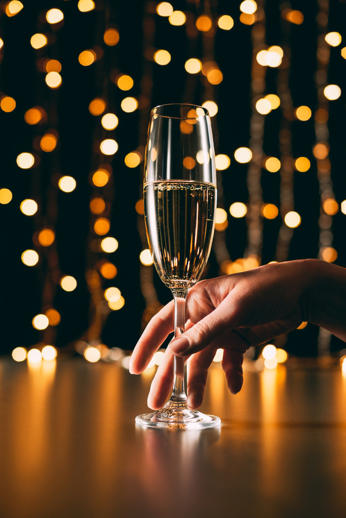 cropped image of woman touching glass of champagne on garland light background, christmas concept - Photo, Image