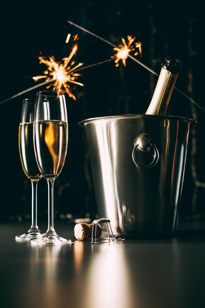 champagnefles in emmer en Kerstmis schittert op donkere achtergrond - Foto, afbeelding