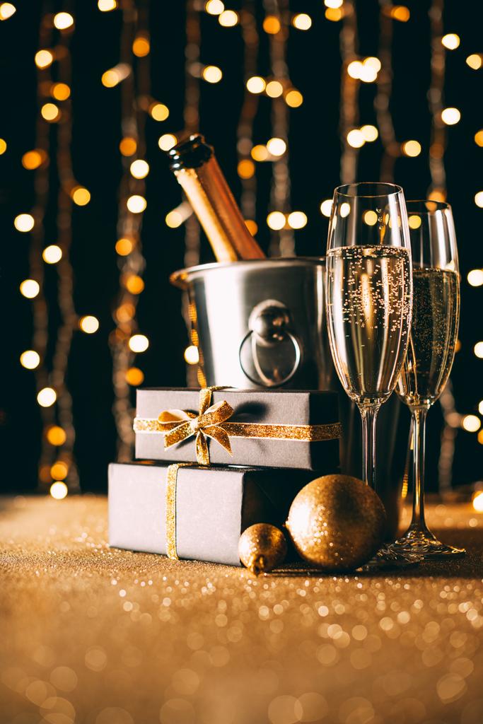 superficie nivel de regalos, copas de champán y bolas sobre fondo claro guirnalda, concepto de Navidad
 - Foto, Imagen