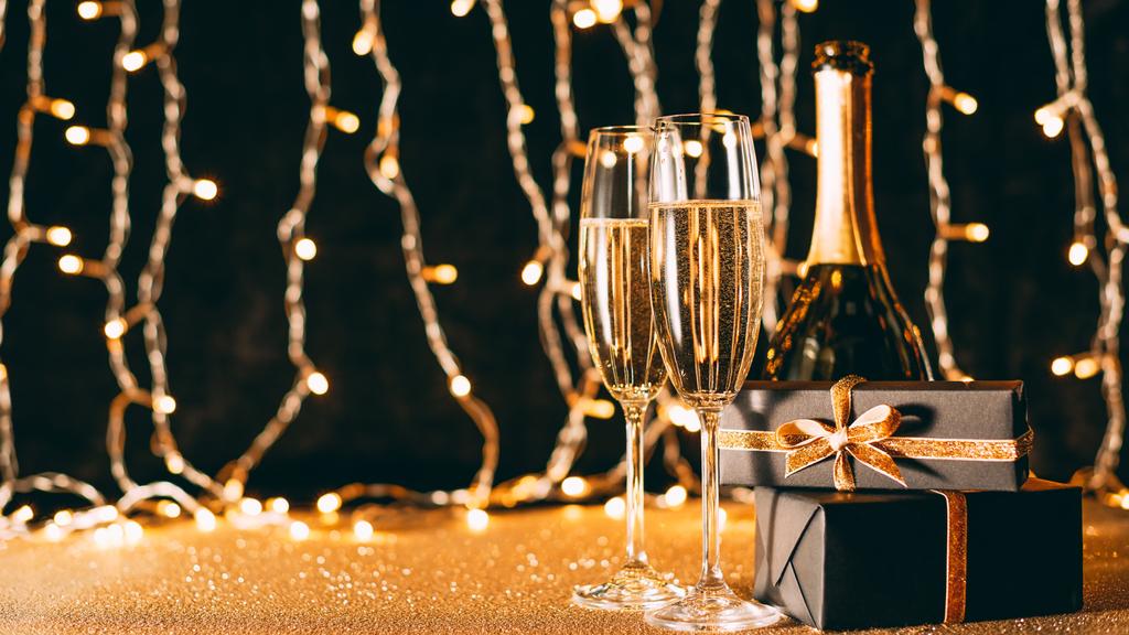two glasses of champagne, presents and bottle on garland light background, christmas concept - Photo, Image