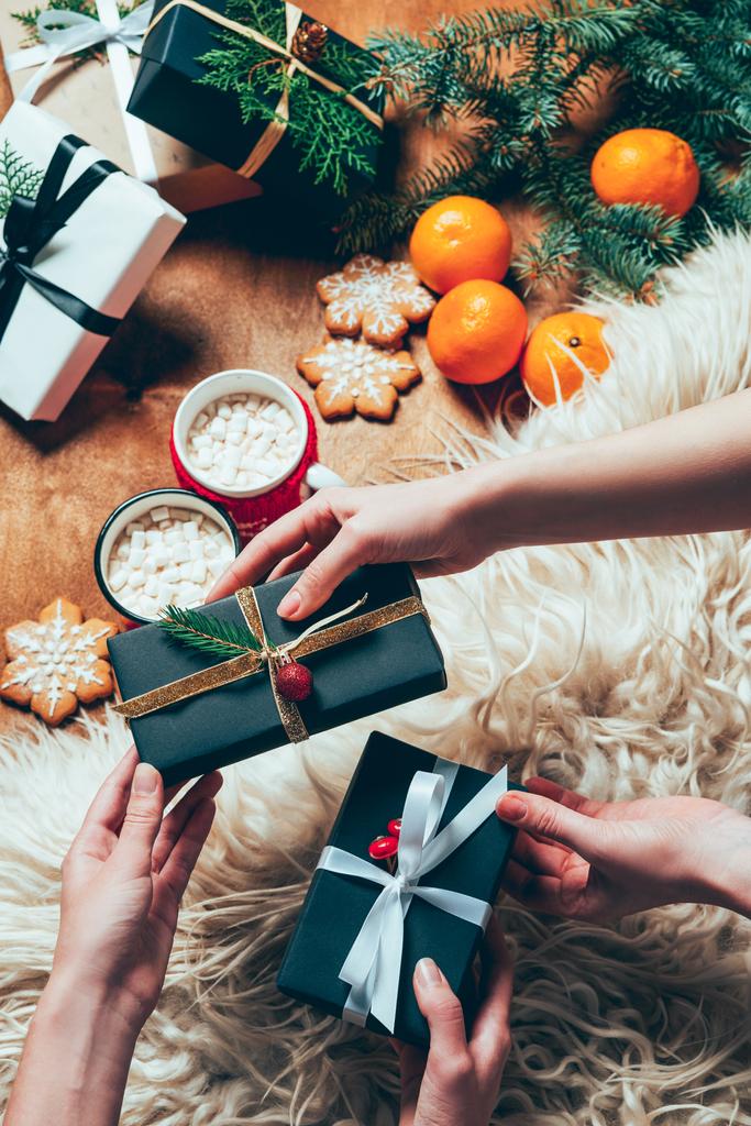 vista parcial de amigos intercambiando regalos de Navidad envueltos en el fondo con tazas de bebidas de cacao y mandarinas
 - Foto, Imagen
