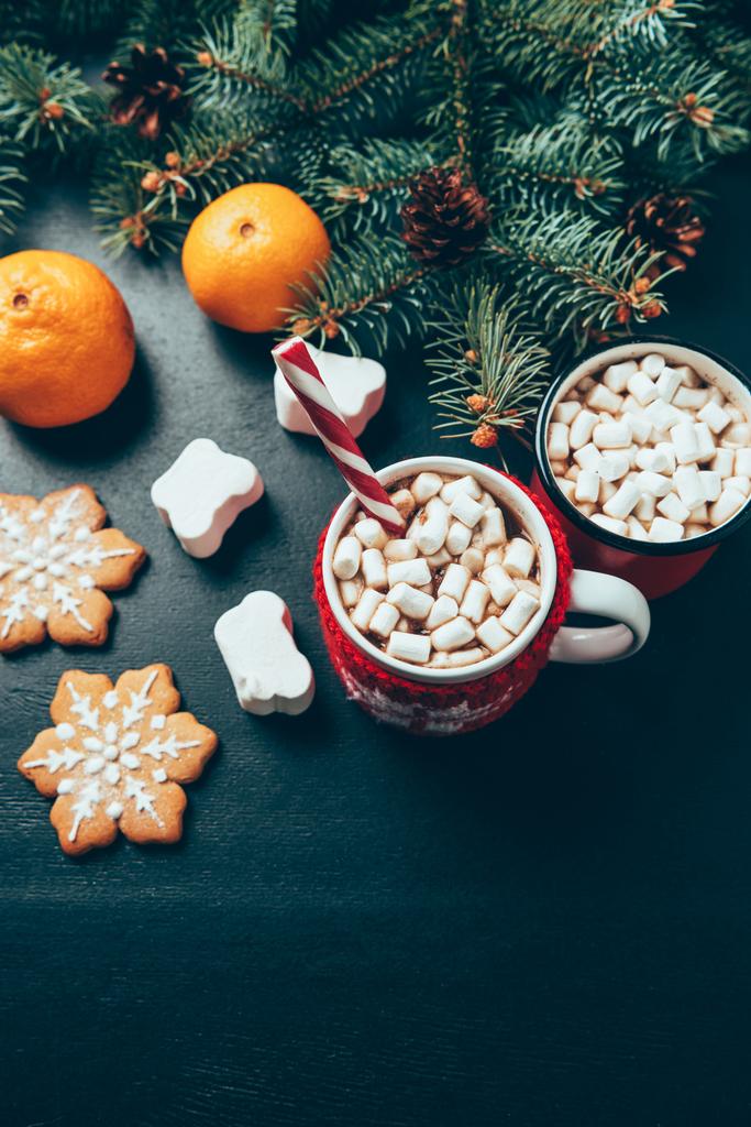 vista dall'alto di tazze di bevande calde con marshmallow, biscotti e mandarini sulla superficie nera, concetto di colazione natalizia
 - Foto, immagini