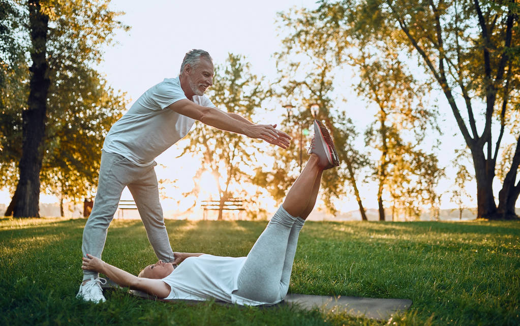 Старшая пара занимается спортом на открытом воздухе. Растягивается в парке на рассвете. Занимаемся йогой вместе. Понятие здорового образа жизни
 - Фото, изображение
