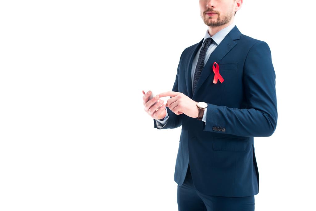 περικομμένη εικόνα του επιχειρηματία με κόκκινη κορδέλα στο κοστούμι χρησιμοποιώντας smartphone που απομονώνονται σε λευκό, world aids Μονοήμερα έννοια - Φωτογραφία, εικόνα