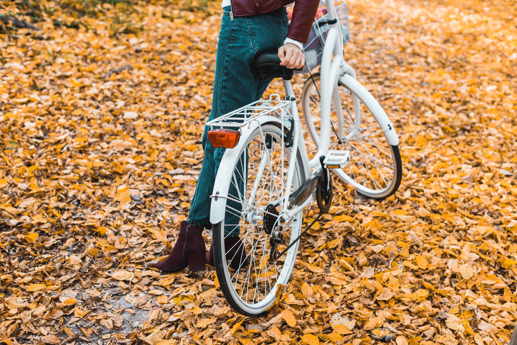 abgeschnittenes Bild einer stilvollen Frau, die in der Nähe von Fahrrad im herbstlichen Wald posiert  - Foto, Bild