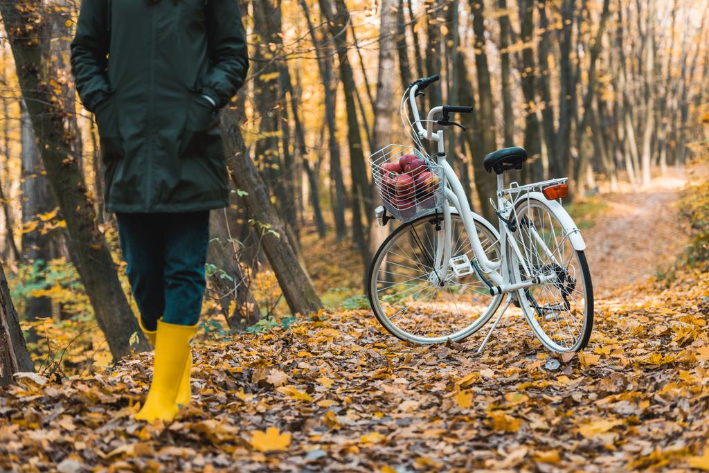 cropped image of woman in yellow gumboots walking near bicycle in autumnal forest - Photo, Image