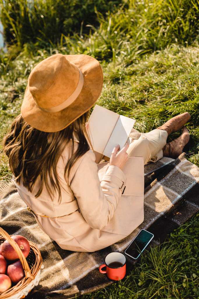 vista posteriore di elegante elegante donna in cappello libro di lettura sulla coperta vicino stagno all'aperto
  - Foto, immagini