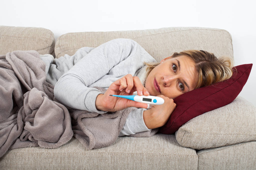 Nuori nainen, jolla on kausiluonteinen flunssa, on päänsärky ja kuume, jotka makaavat sohvalla käärittynä balnketiin.
 - Valokuva, kuva