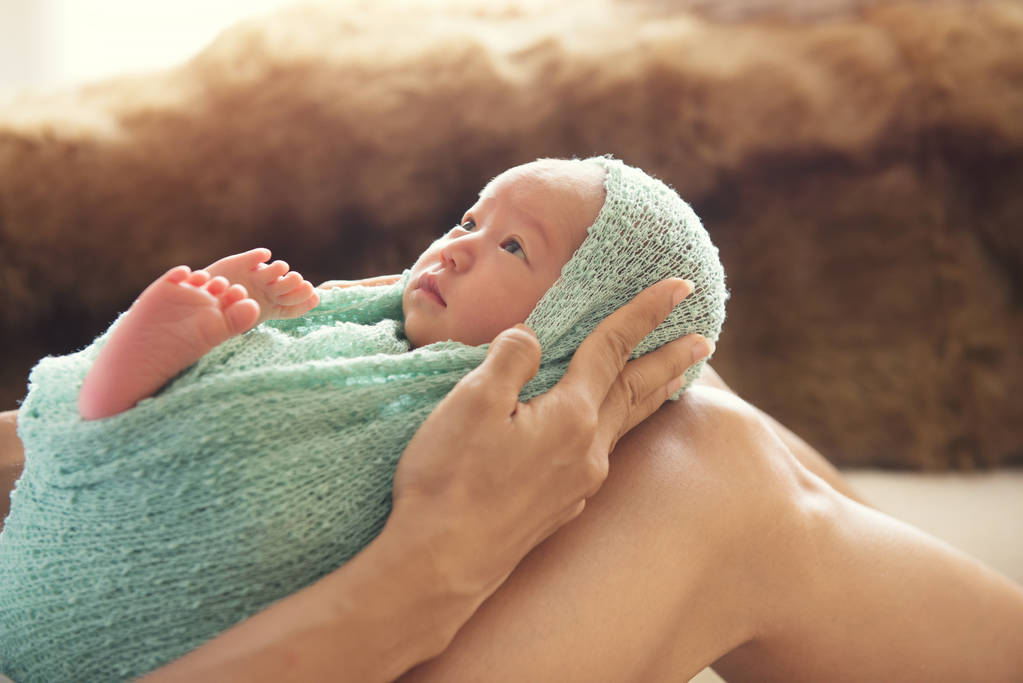 Yeni doğan bebek yeşil kumaş sarma bacaklarının üzerinde tutan kadın - Fotoğraf, Görsel