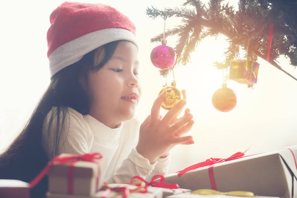 Досить мало щаслива дівчина Азії і посмішка в Санта cap біла сорочка поблизу Різдво дерево мають багато подарунковій коробці - Фото, зображення