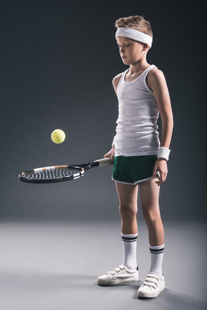 Preteen jongen in sportkleding met tennisracket en bal op donkere achtergrond - Foto, afbeelding