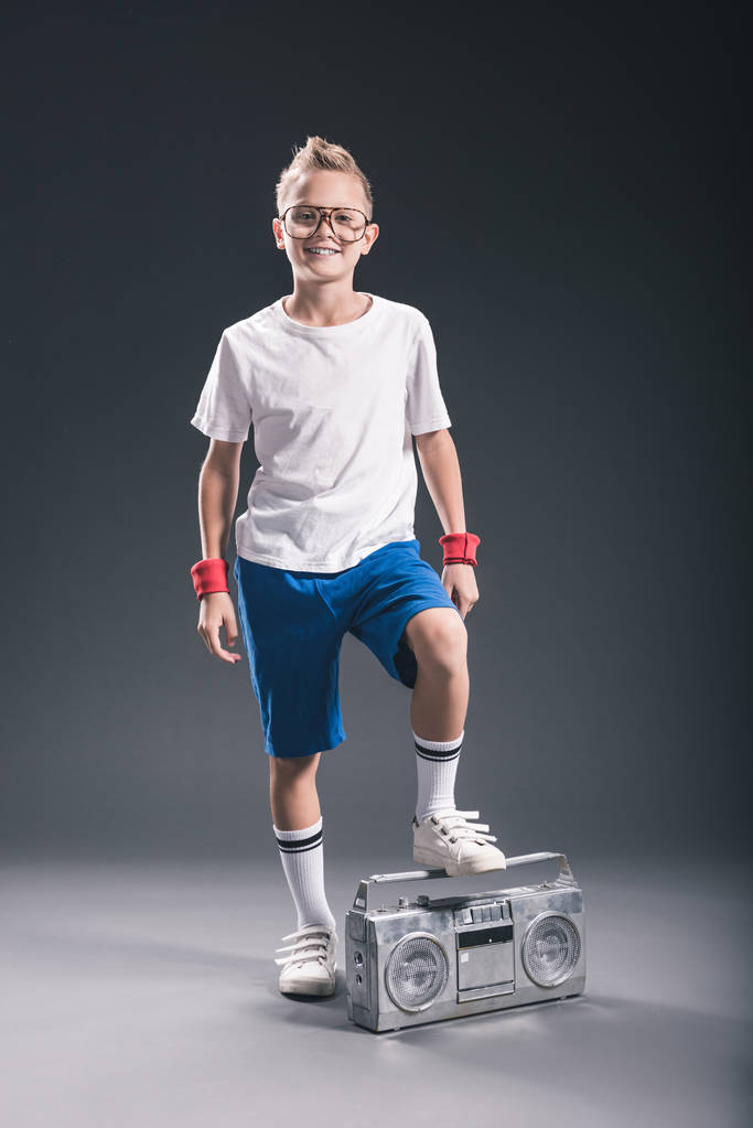 smiling preteen boy in eyeglasses with boombox posing on grey backdrop - Photo, Image