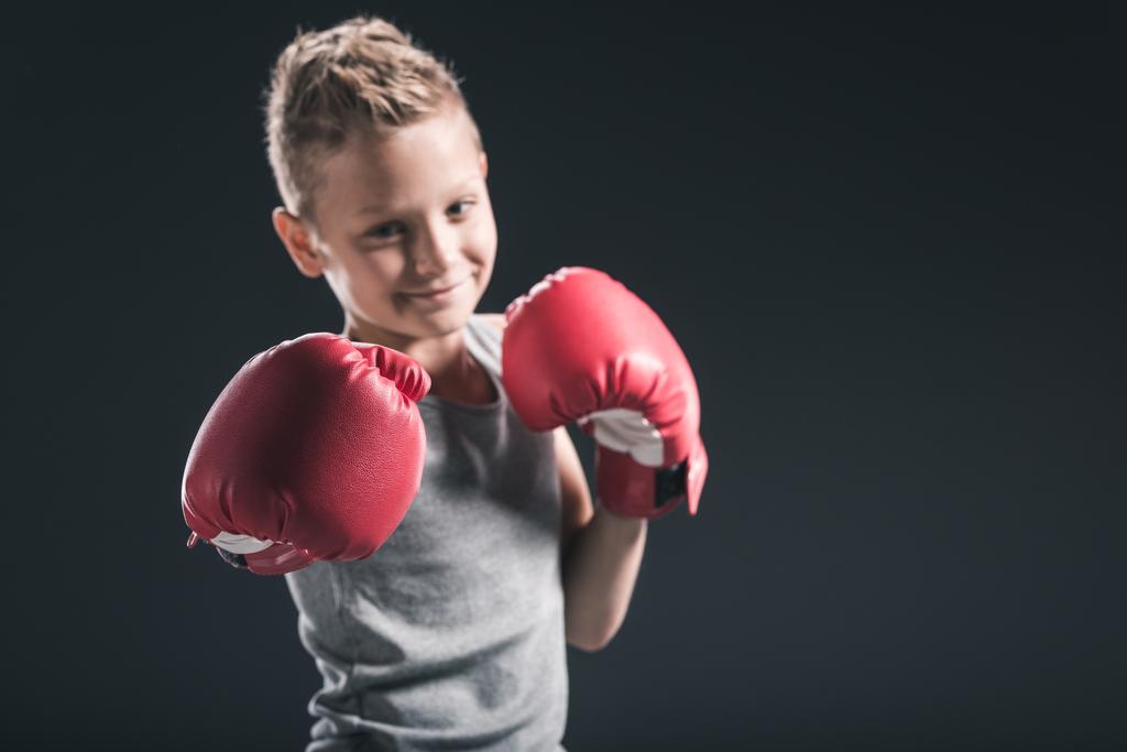 portrait of smiling boy with red boxing gloves on black backdrop - Photo, Image