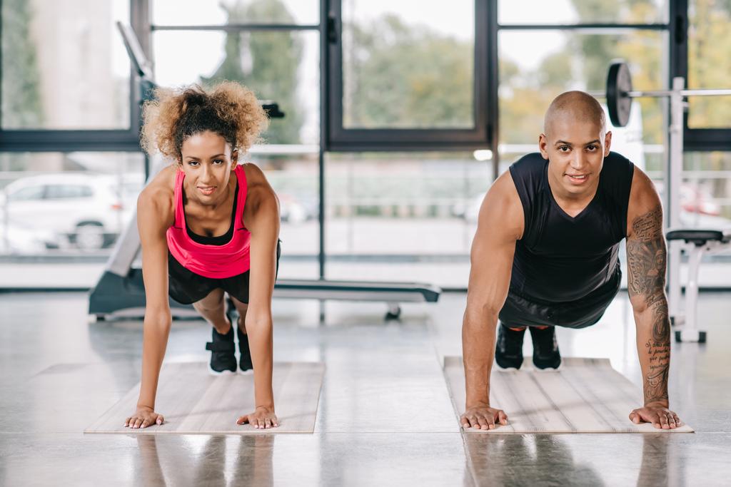 feliz jovem Africano americano casal de atletas fazendo prancha em tapetes de fitness no ginásio
 - Foto, Imagem