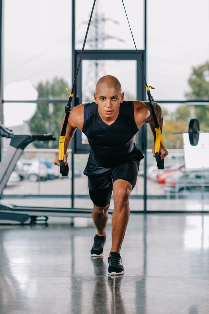 focused african american sportsman exercising on fitness straps at gym - Photo, Image