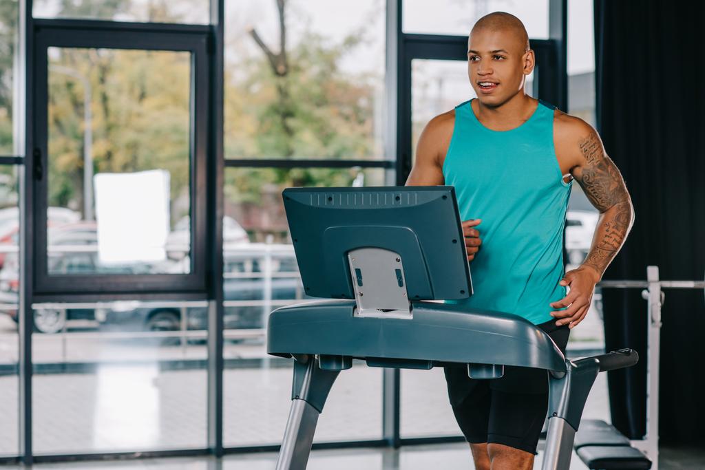muskulöser afrikanisch-amerikanischer Sportler mit tätowierter Hand beim Laufen auf dem Laufband im Fitnessstudio - Foto, Bild