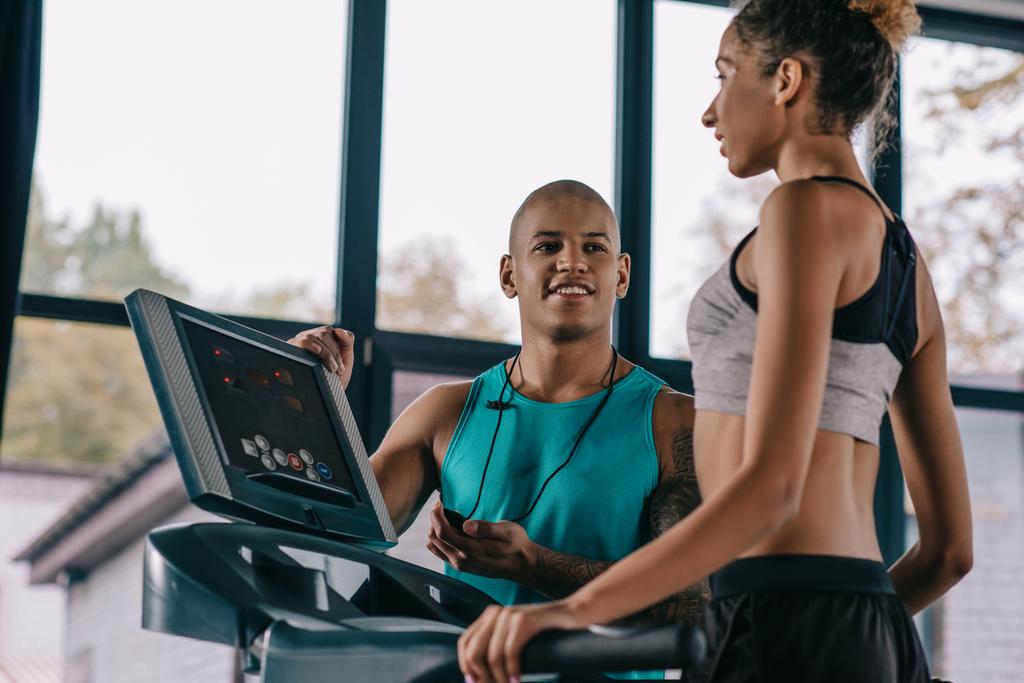 young male trainer with timer looking at sportswoman running on treadmill at gym - Photo, Image