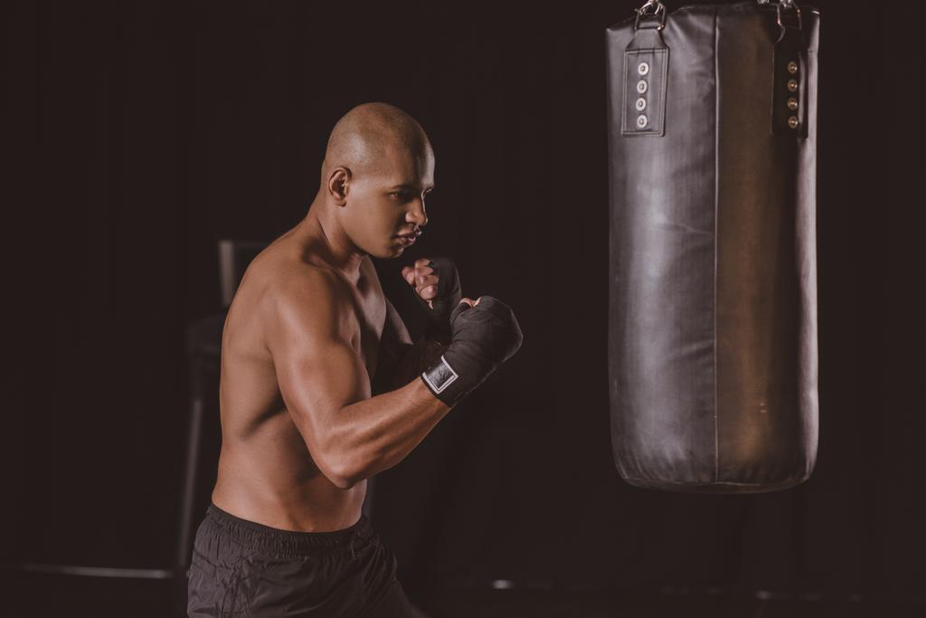 kum torbası vasıl jimnastik salonu ile eğitim boks bandaj genç Afro-Amerikan erkek boksör - Fotoğraf, Görsel