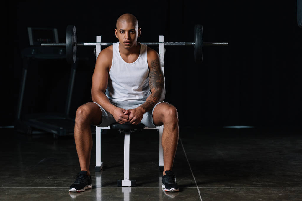 serious african american male athlete looking at camera and sitting at gym - Photo, Image