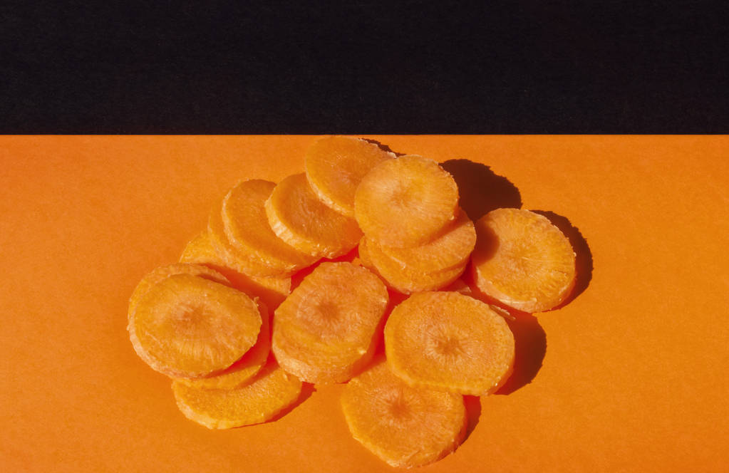 Ένα όμορφο μάτσο κομμένα σε φέτες καρότα σε έγχρωμο φόντο, το top view, studio που γυρίστηκε, πορτοκαλί και μαύρο χρώμα αρμονία - Φωτογραφία, εικόνα