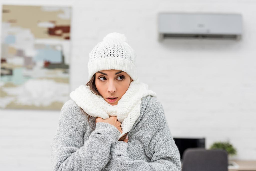 close-up portrait of freezing young woman in warm clothes with air conditioner on background - Photo, Image