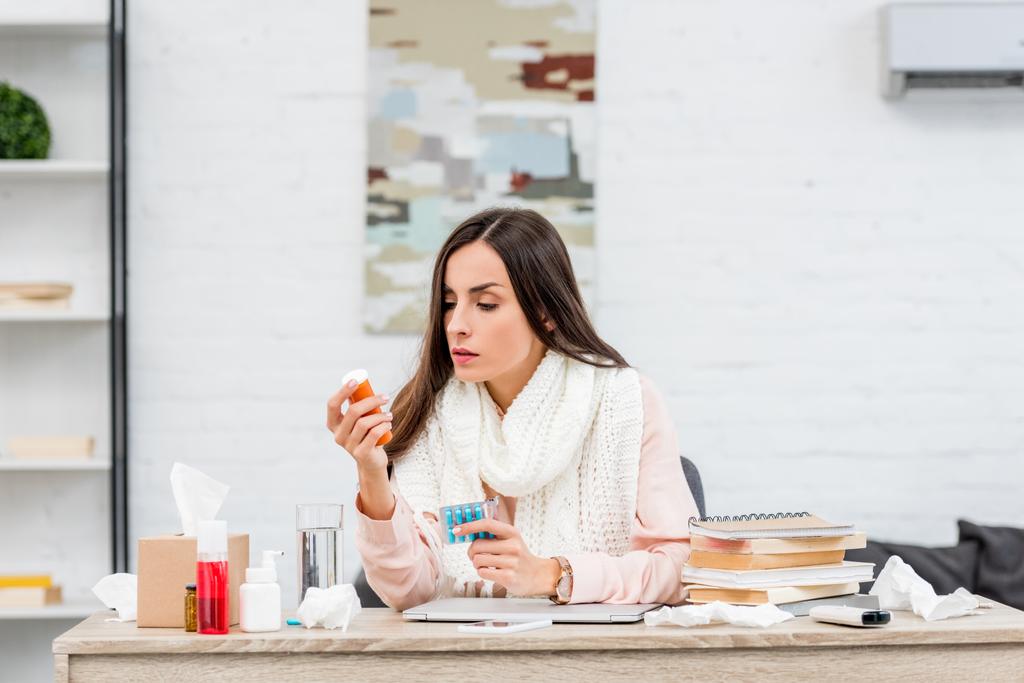 joven mujer de negocios enferma sosteniendo medicamentos mientras está sentada en el lugar de trabajo
 - Foto, Imagen
