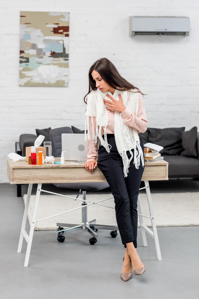 хвора молода бізнес-леді н шарф спираючись на робоче місце в офісі
 - Фото, зображення