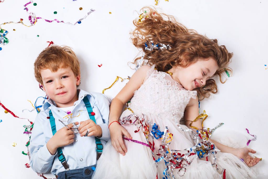 Divertida chica feliz y niño pequeño celebrando fiesta de cumpleaños, sonriendo y acostado en confeti multicolor
 - Foto, imagen