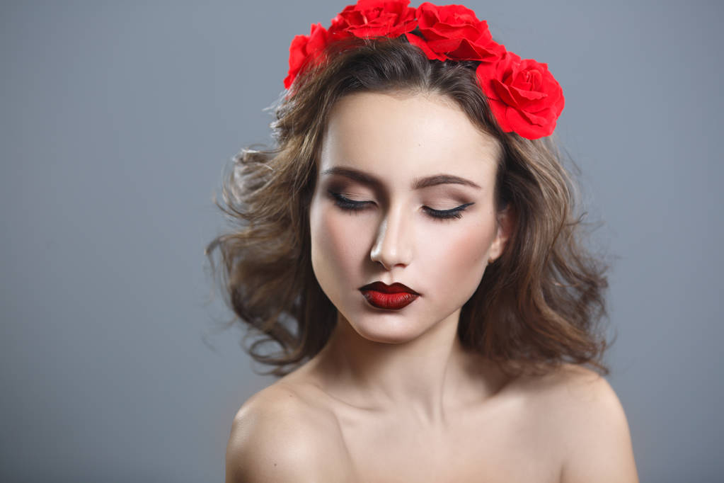 Portret van de schoonheid van een mooie vrouw met rode lippenstift en een decoratieve krans op een grijze achtergrond. - Foto, afbeelding