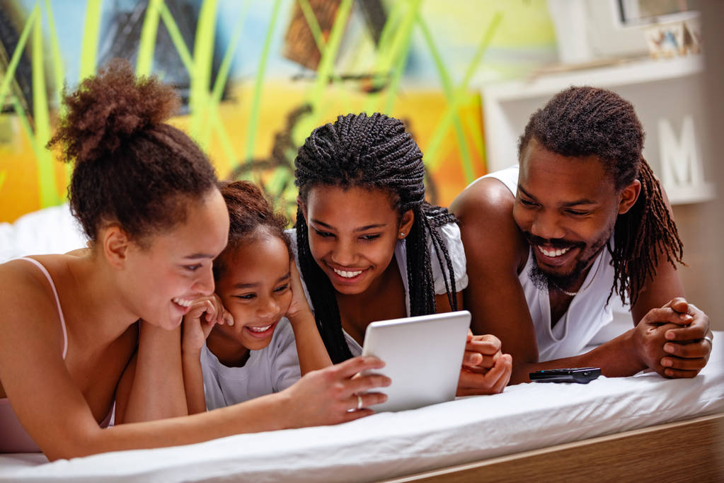 Sorridente famiglia afroamericana utilizzando tablet mentre sdraiati insieme sul letto
 - Foto, immagini