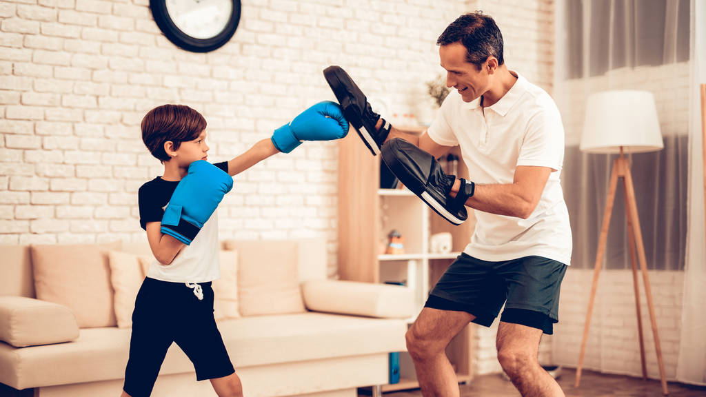 Boy Boxer. Father and Son do Spotting. Sport at Home. Warm Up in Quarter. Tablet in Hands. Boxing Gloves. Doing Sports. Man and Boy Train at Home. Child in Boxing Gloves in Apartment. Little Boy. - Photo, Image
