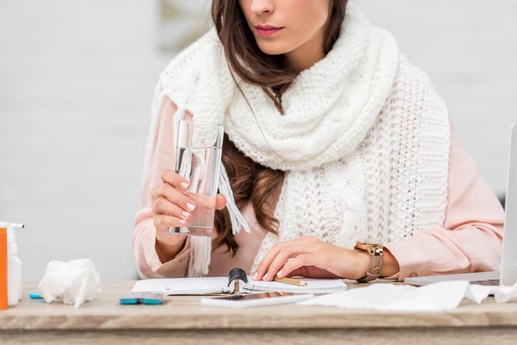 cropped shot of sick young woman in scarf holding glass of water at workplace - Photo, Image