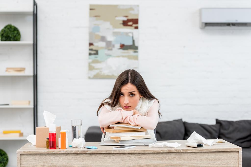 sick young businesswoman leaning on stack of books at workplace and looking at camera - Photo, Image