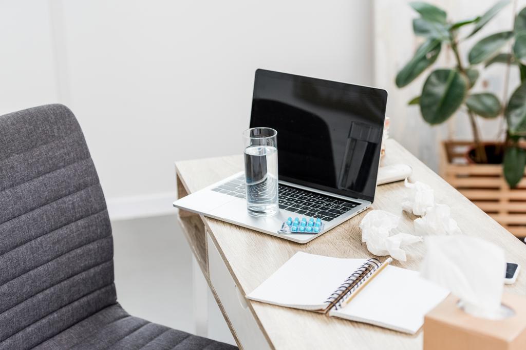 irodai munkahely laptop, pohár vizet és a buborékcsomagoláson tabletták - Fotó, kép