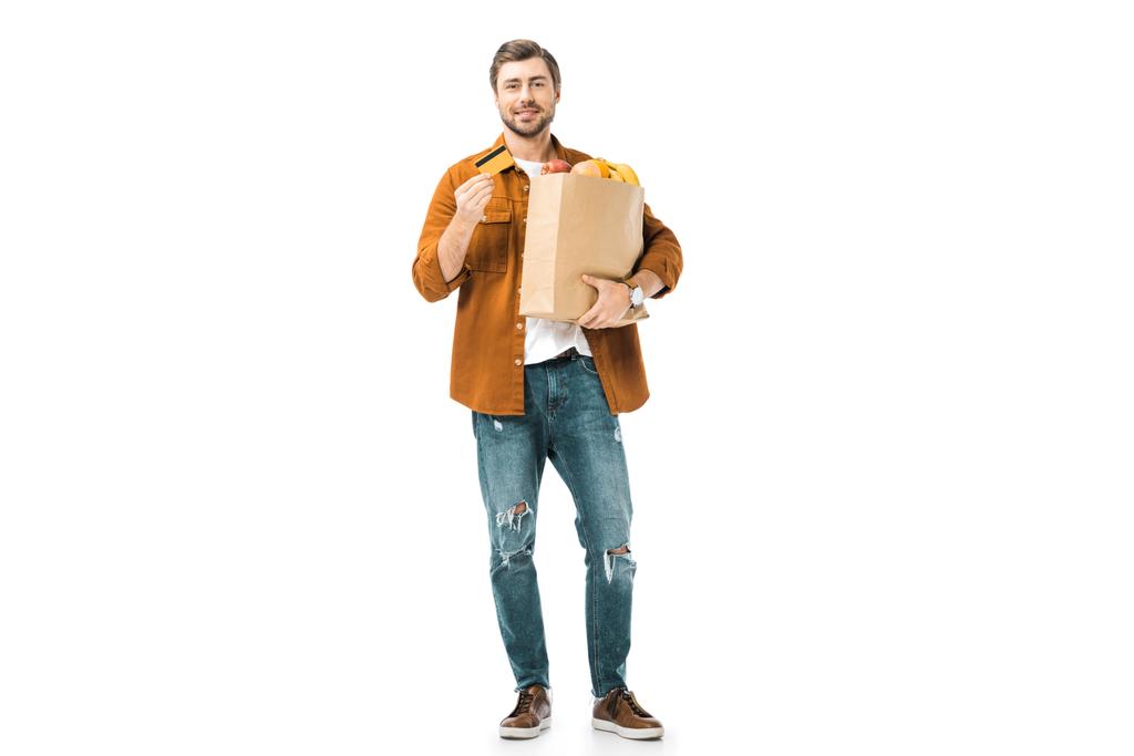 glücklicher Mann mit Einkaufstasche voller Produkte, die Kreditkarte isoliert auf weiß zeigen - Foto, Bild