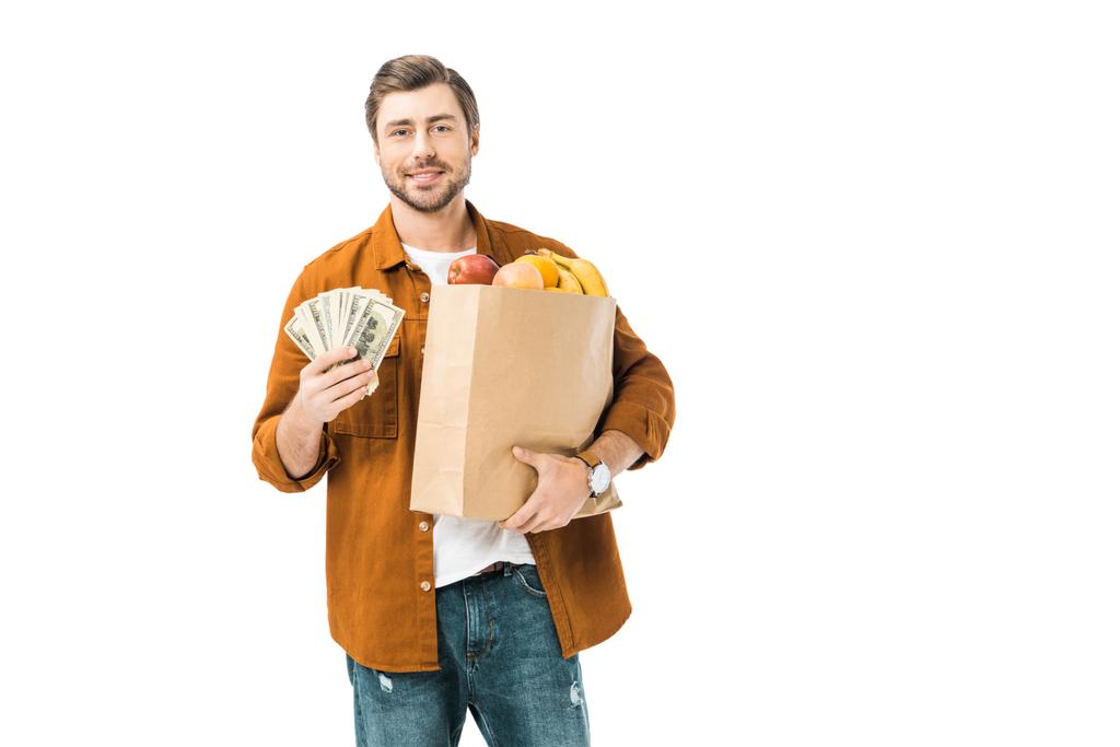 ευτυχισμένος άνθρωπος δείχνει μετρητά χρήματα και κρατώντας πλήρη προϊόντα απομονώνονται σε λευκό χαρτί τσάντα - Φωτογραφία, εικόνα