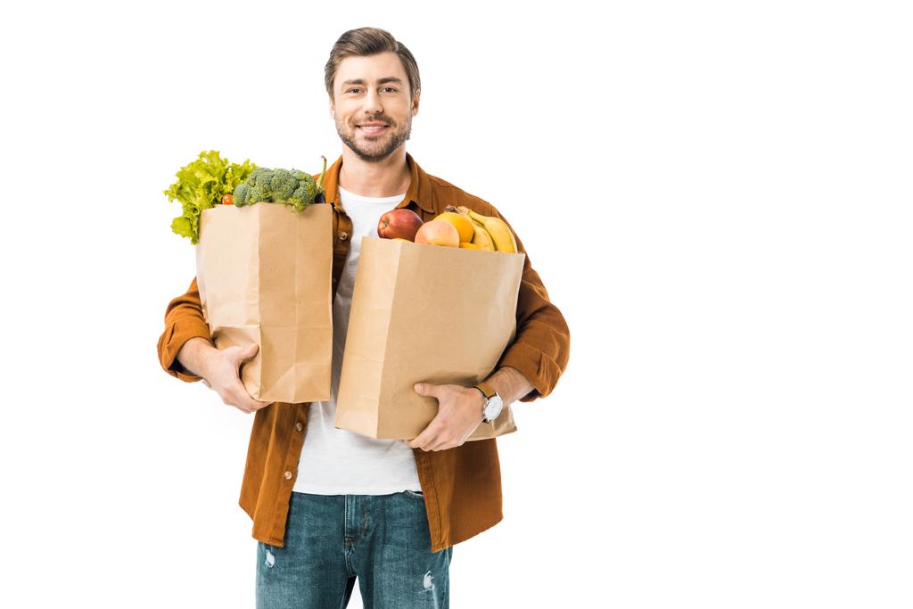 cheerful man holding paper bags full of products isolated on white - Photo, Image