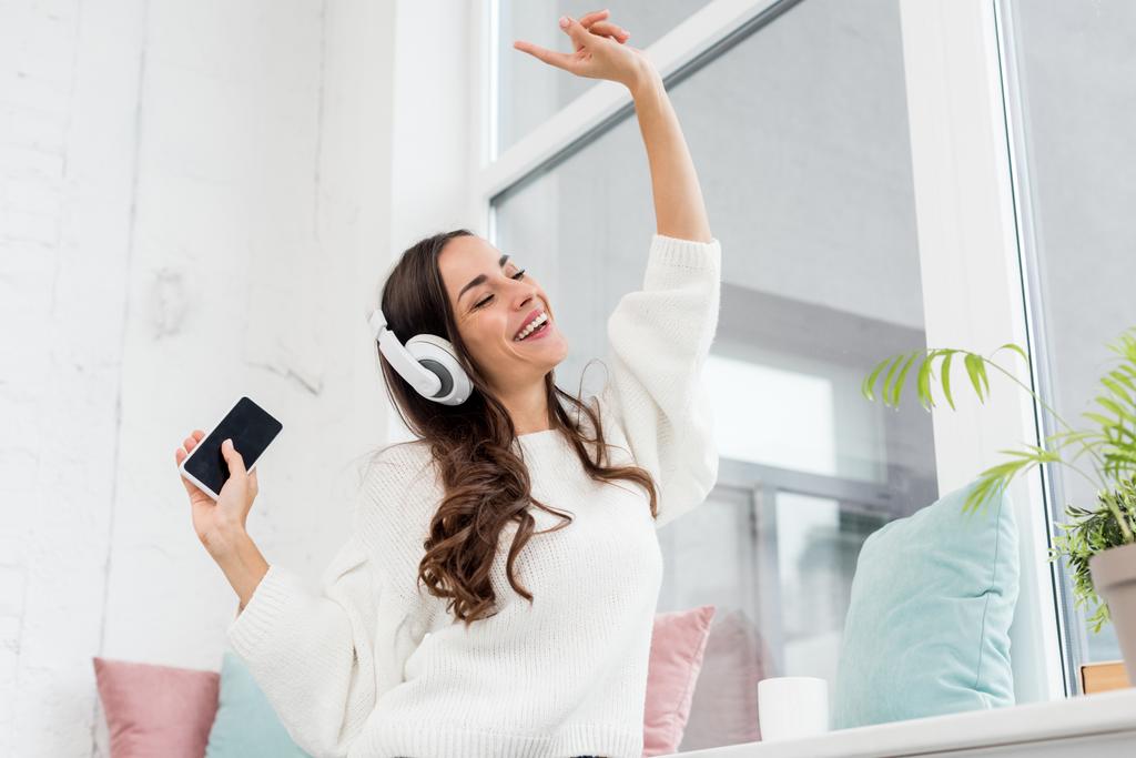bottom view of happy young woman listening music with smartphone and wireless headphones at home - Photo, Image