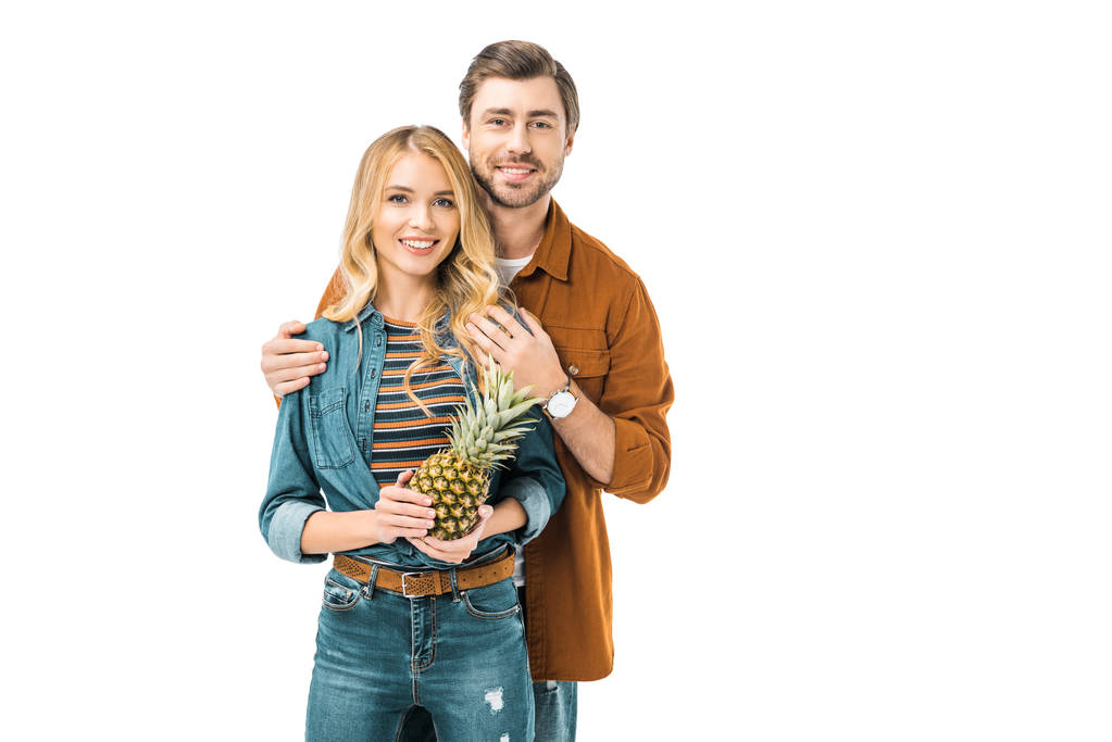 muž všeobjímající šťastný přítelkyně, zatímco ona drží ananas izolované na bílém  - Fotografie, Obrázek