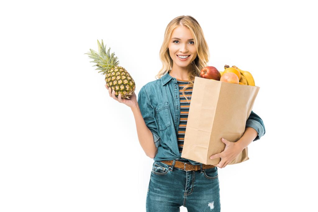 portrait of young woman holding pineapple and paper bag with products isolated on white - Photo, Image