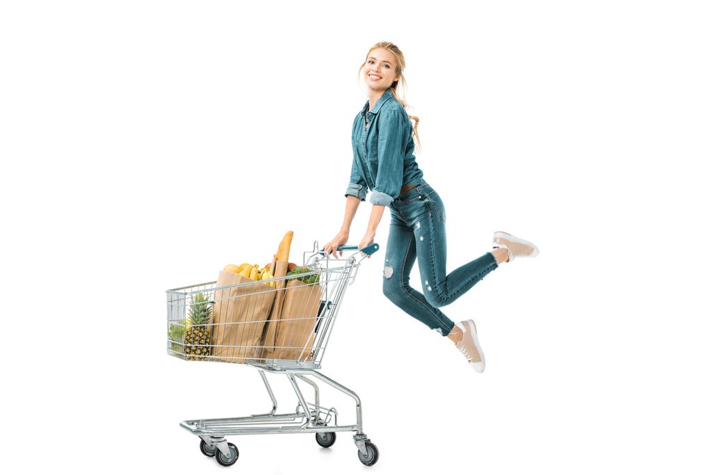 紙袋白で隔離の商品とトロリーのショッピングカート近くジャンプ幸せな若い女 - 写真・画像