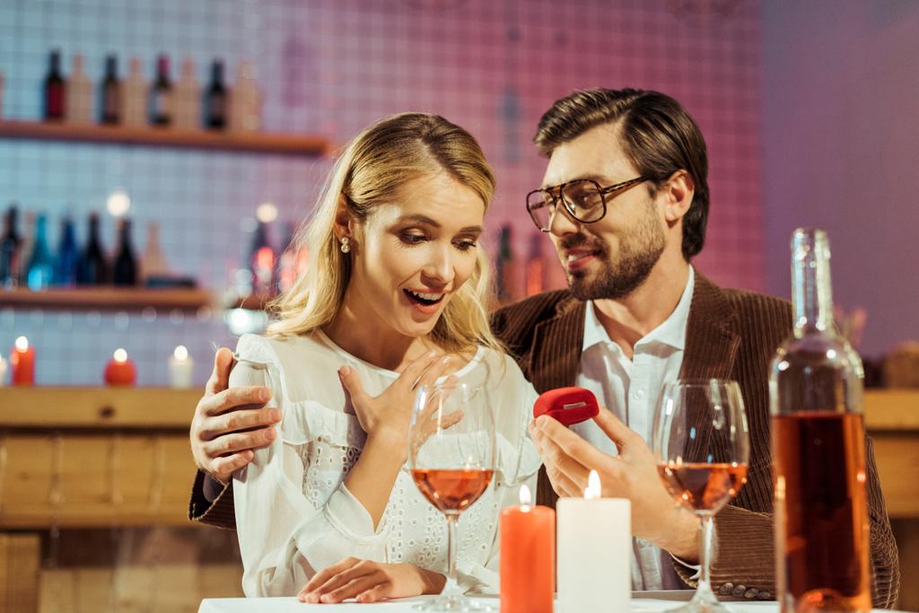 glücklicher junger Mann macht seiner schönen Freundin während eines romantischen Abendessens im Café einen Heiratsantrag - Foto, Bild