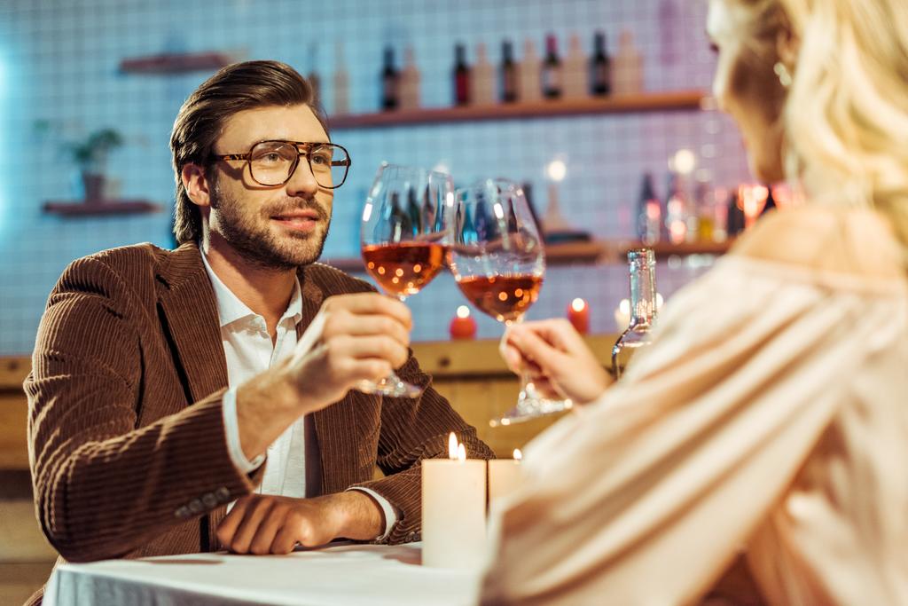 szelektív összpontosít, a fiatal pár ünnepli, és az asztalnál a gyertyák étteremben borospohár csengő  - Fotó, kép