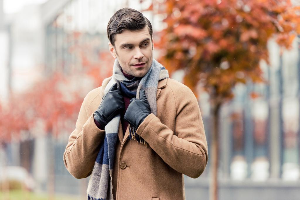 стильный мужчина в пальто, кожаных перчатках и шарфе стоит на осенней улице
 - Фото, изображение