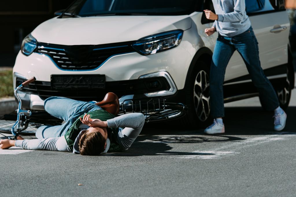 bijgesneden schot van vrouw loopt naar de gewonde wielrenner bij verkeersongeval  - Foto, afbeelding