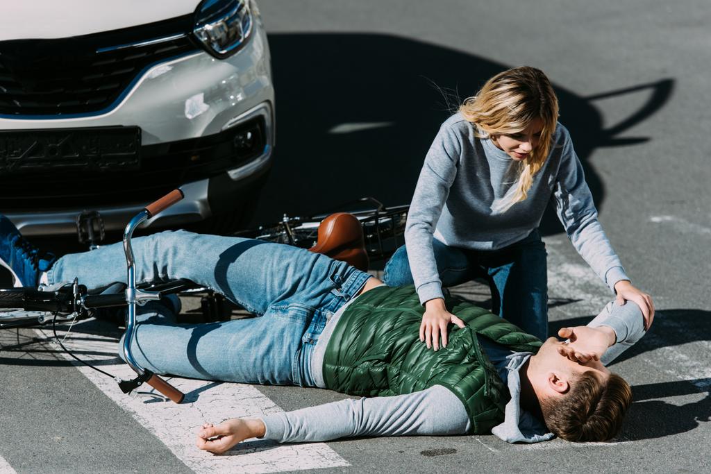 Frau sieht verletzten jungen Radfahrer, der bei Autounfall mit Fahrrad auf Straße liegt - Foto, Bild