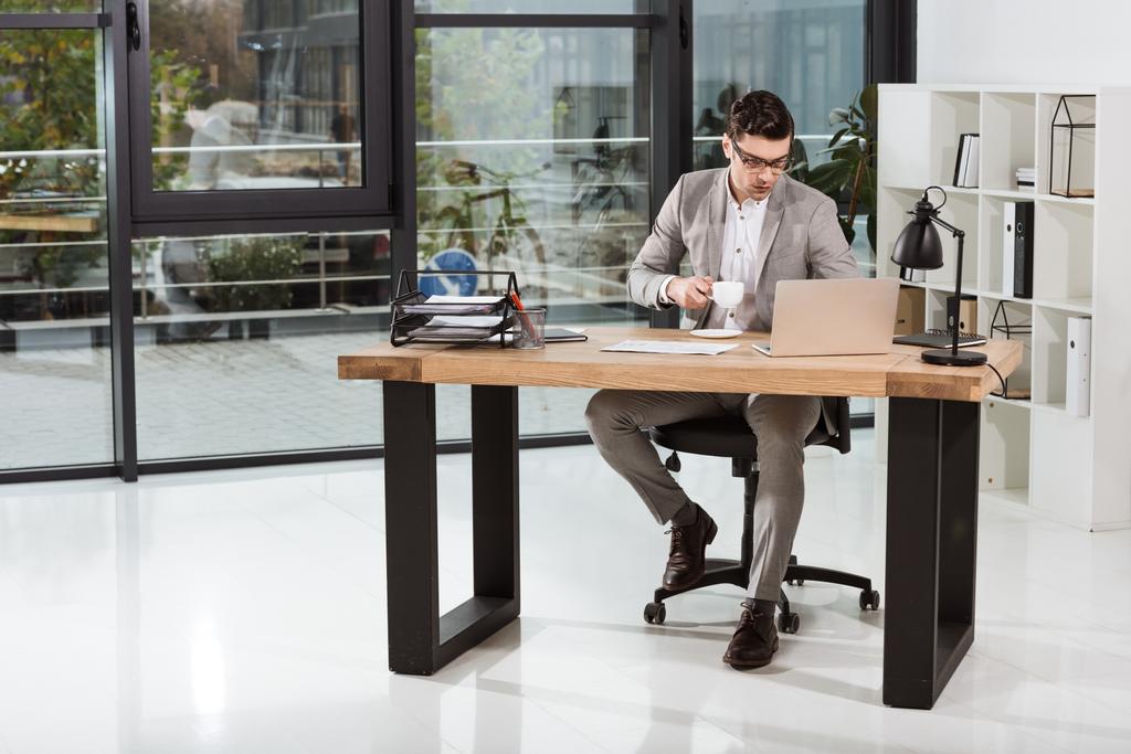 jóképű üzletember csésze kávéval működő laptop iroda - Fotó, kép