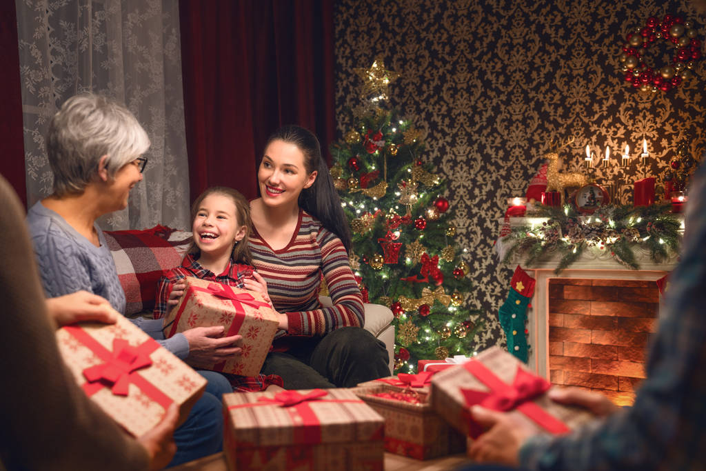 Merry Christmas and Happy Holidays! Grandma, grandpa, mum, dad and child exchanging gifts. Parents and daughter having fun near tree indoors. Loving family with presents in room. - Photo, Image