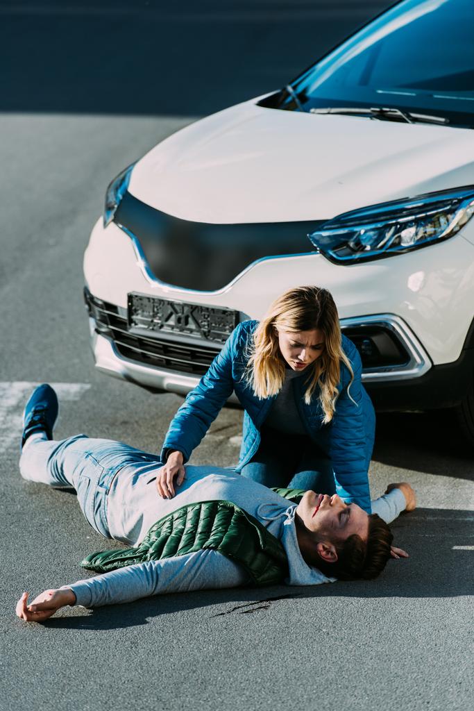 vue en angle élevé de la jeune femme regardant toucher un homme blessé allongé sur la route après un accident de la circulation
 - Photo, image