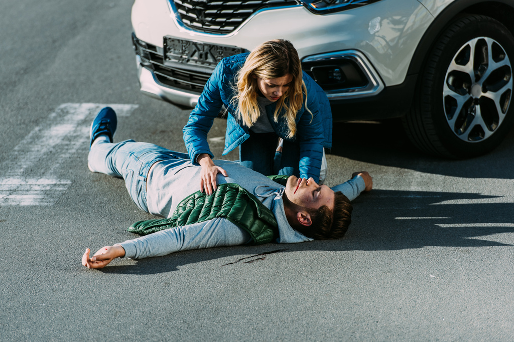 vue grand angle de la jeune femme effrayée touchant homme blessé couché sur la route après un accident de voiture
 - Photo, image